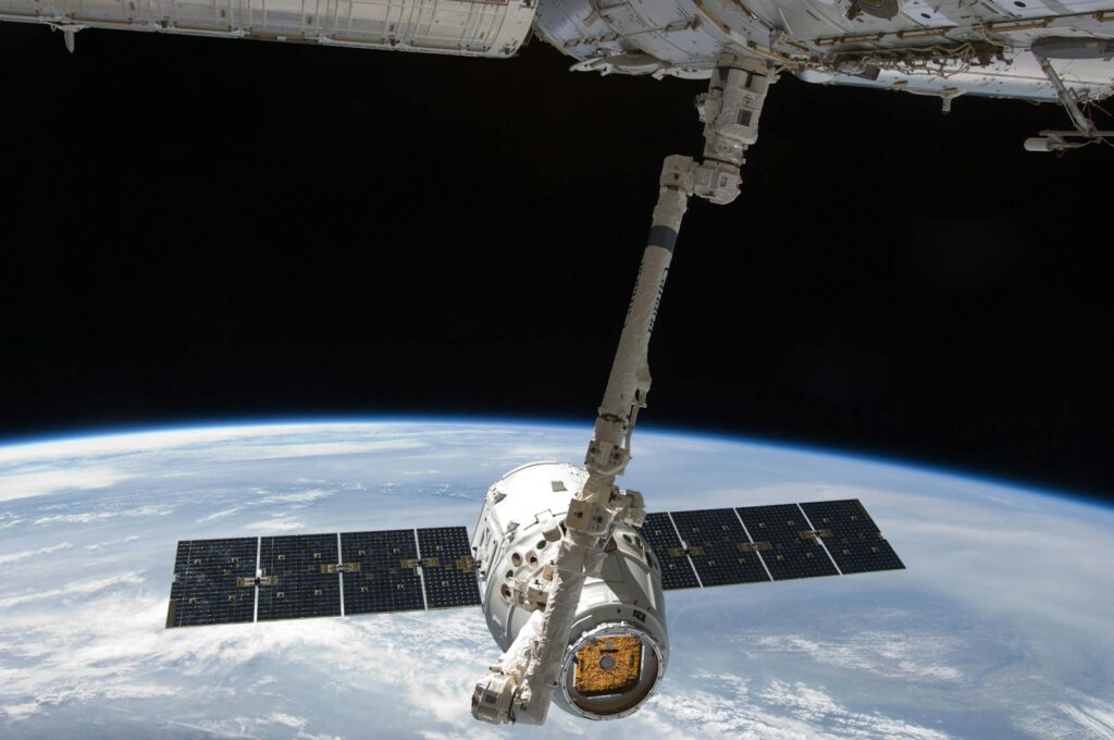 View of a spacecraft docked at the ISS above Earth with visible solar panels.