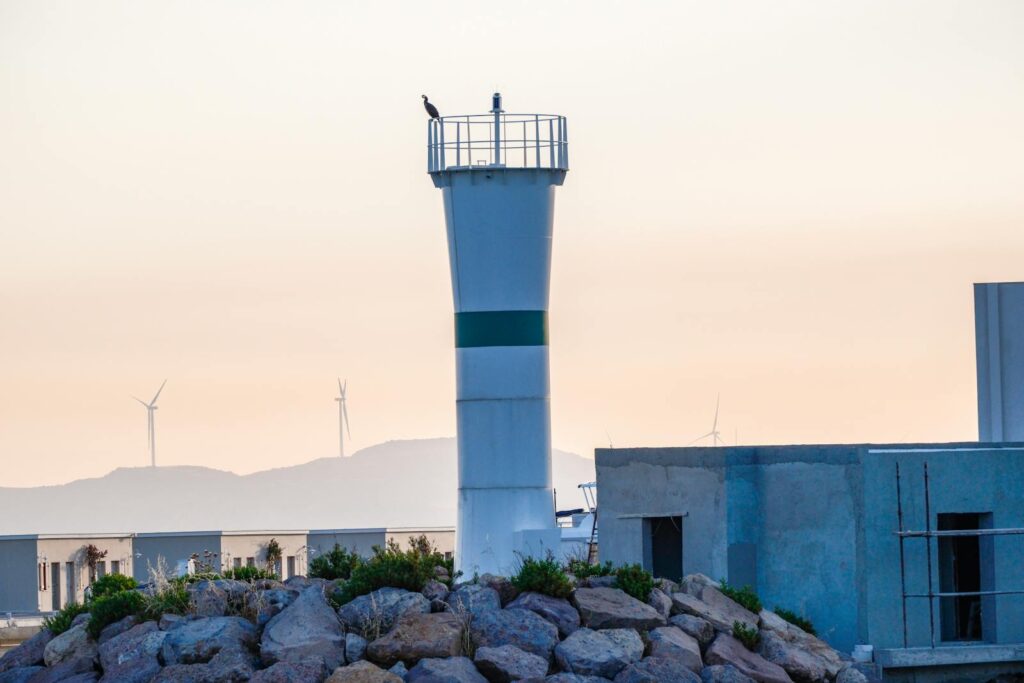 Serene lighthouse scene during sunset in Foça, İzmir, with distant wind turbines.