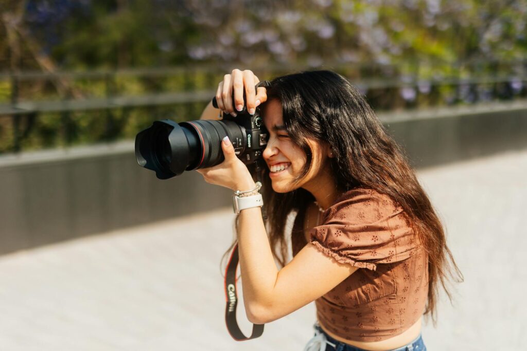 Smiling young woman captures a moment outdoors with a DSLR camera, embracing her passion.
