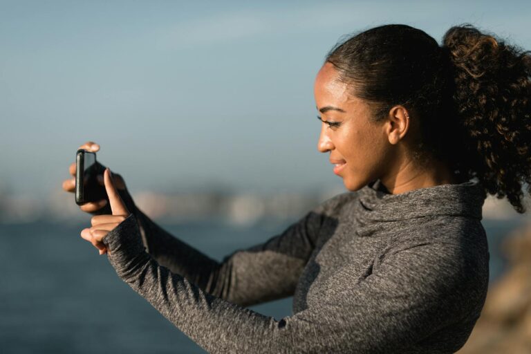 A women smiling while taking a photo of a bird with her smartphone.