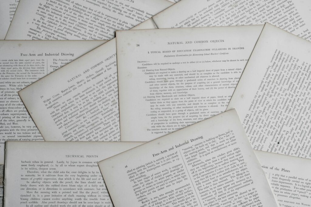 Shows several open pages from older books or examination papers scattered on a surface.