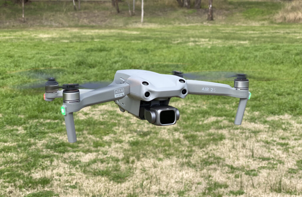 A grey DJI Air 2S drone hovers over green grass.