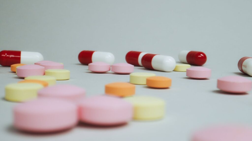 Close-up of varied pills and capsules scattered on a white surface.