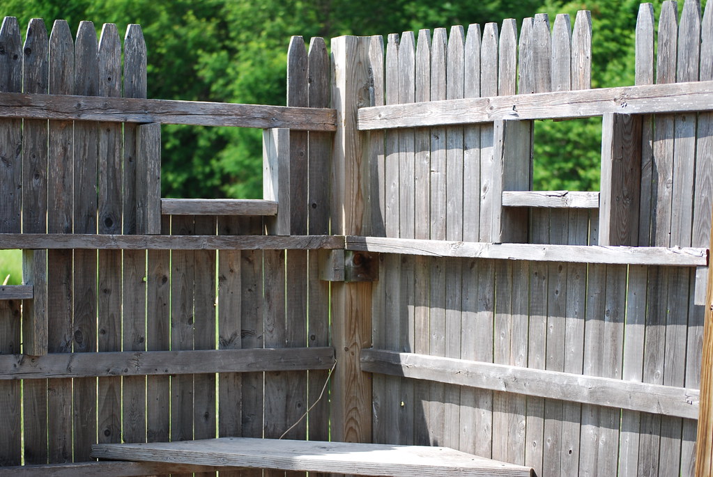 Weathered wooden fence with missing planks reveals greenery beyond.