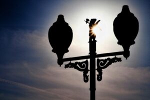 A silhouette of a streetlamp with a bear figure is backlit by a bright sky.