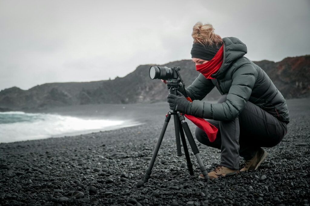 A photographer uses a camera on a tripod at a rocky beach, potentially for birding.