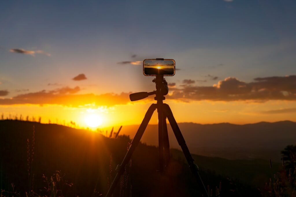 A camera on a tripod with the sun setting in the background.