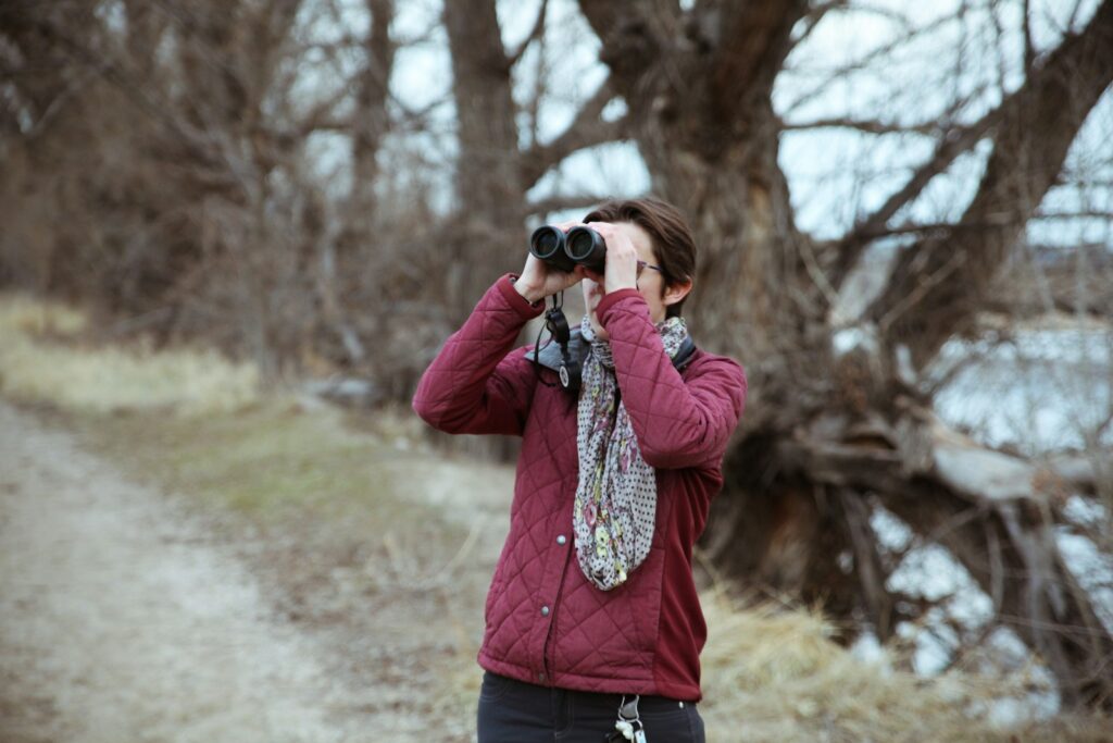 A person uses binoculars for birdwatching, in an outdoor setting.