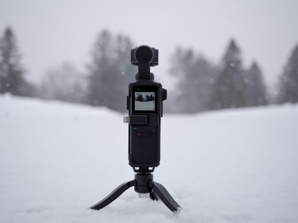 A camera is mounted on a mini tripod in a snowy environment.