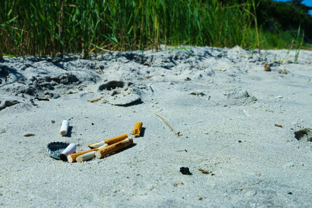 Several discarded cigarette butts and a metal bottle cap scattered on light-colored sand.