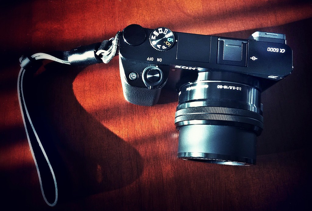 A black Sony Alpha 6000 camera with a lens is placed on a reddish-brown surface.