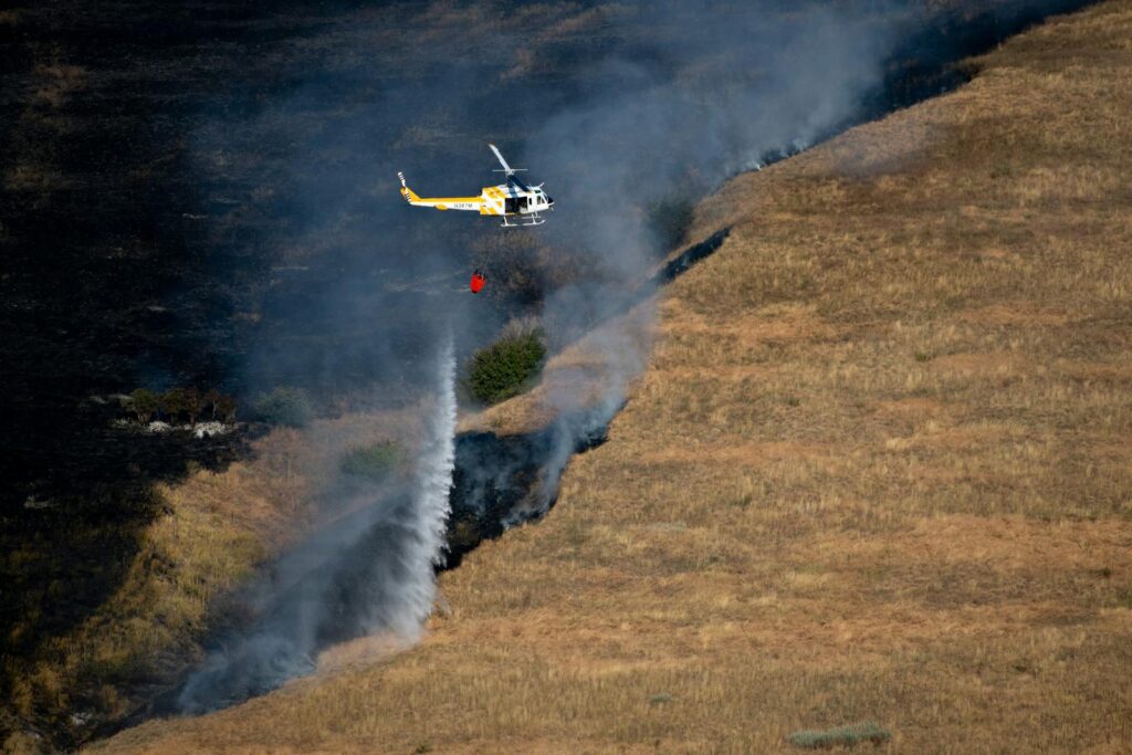 A helicopter is extinguishing a wildfire in a grassy field.