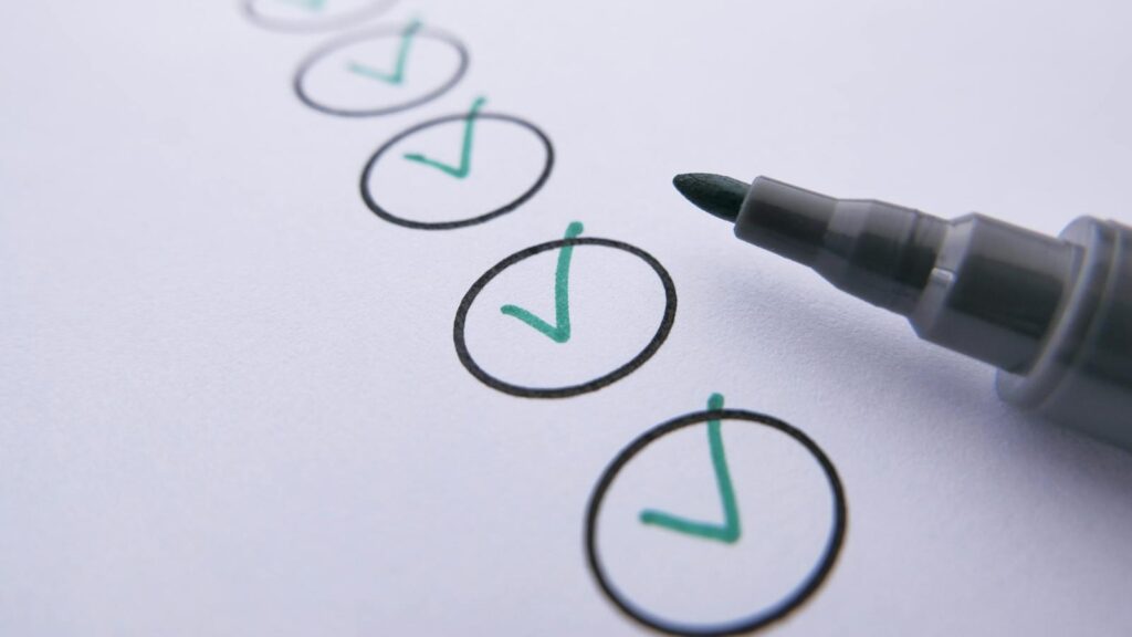 Close-up of a checklist with green checkmarks on white paper using a marker.