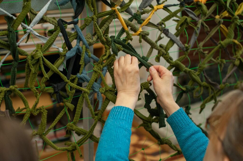 Two hands skillfully weaving a camouflage net, close-up view in an indoor setting.