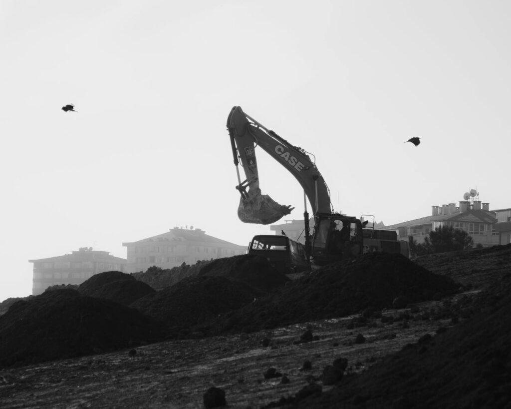 Black and white image of a bulldozer at a construction site with birds in the sky.