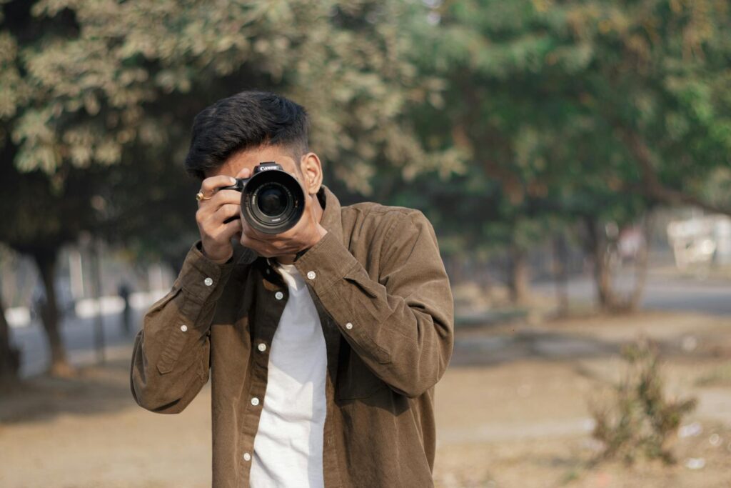 Young man with DSLR camera capturing moments outdoors on a sunny day.