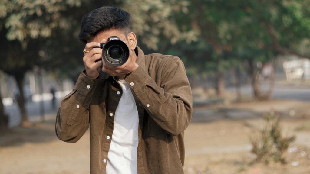 Young man with DSLR camera capturing moments outdoors on a sunny day.