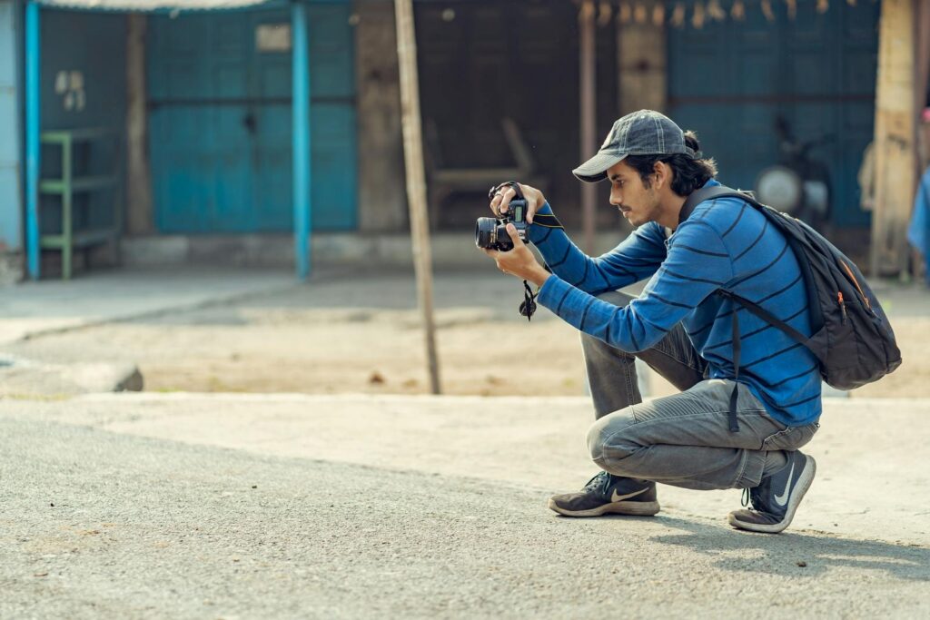 A young man crouching to take photos with his DSLR camera in an urban environment.