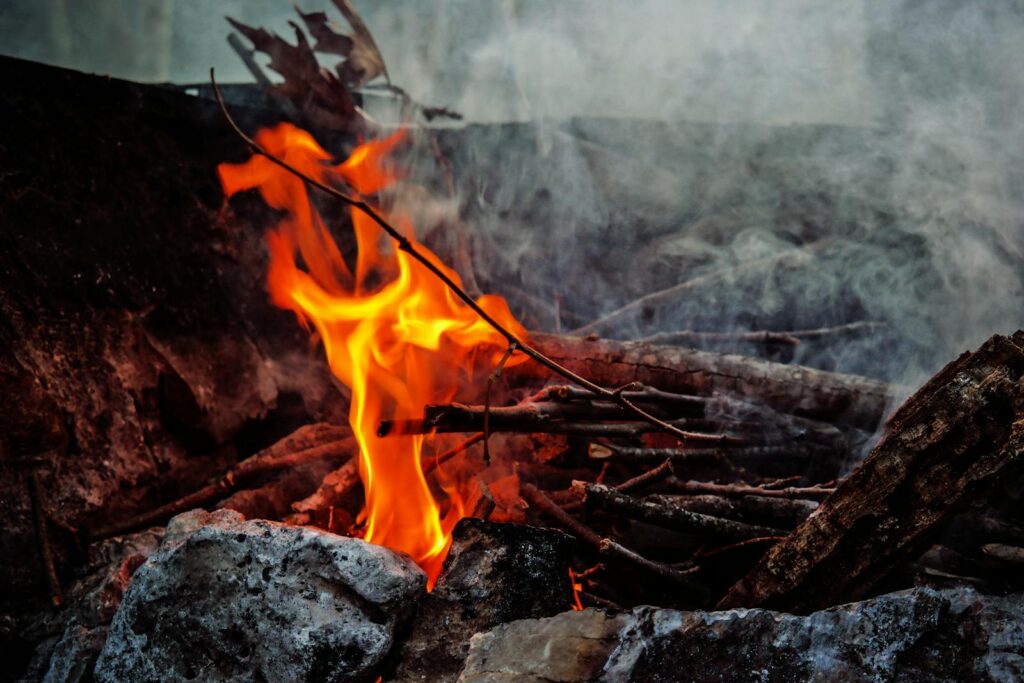 A close-up shot of a campfire with dancing flames and smoke surrounded by logs and stones.