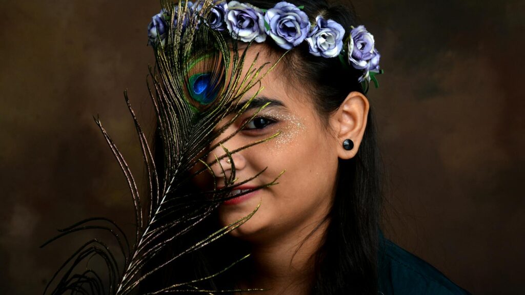 Artistic portrait of a woman wearing a floral wreath, holding a peacock feather as a prop