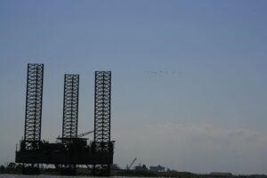 A flock of birds flies in the sky above a large oil rig.