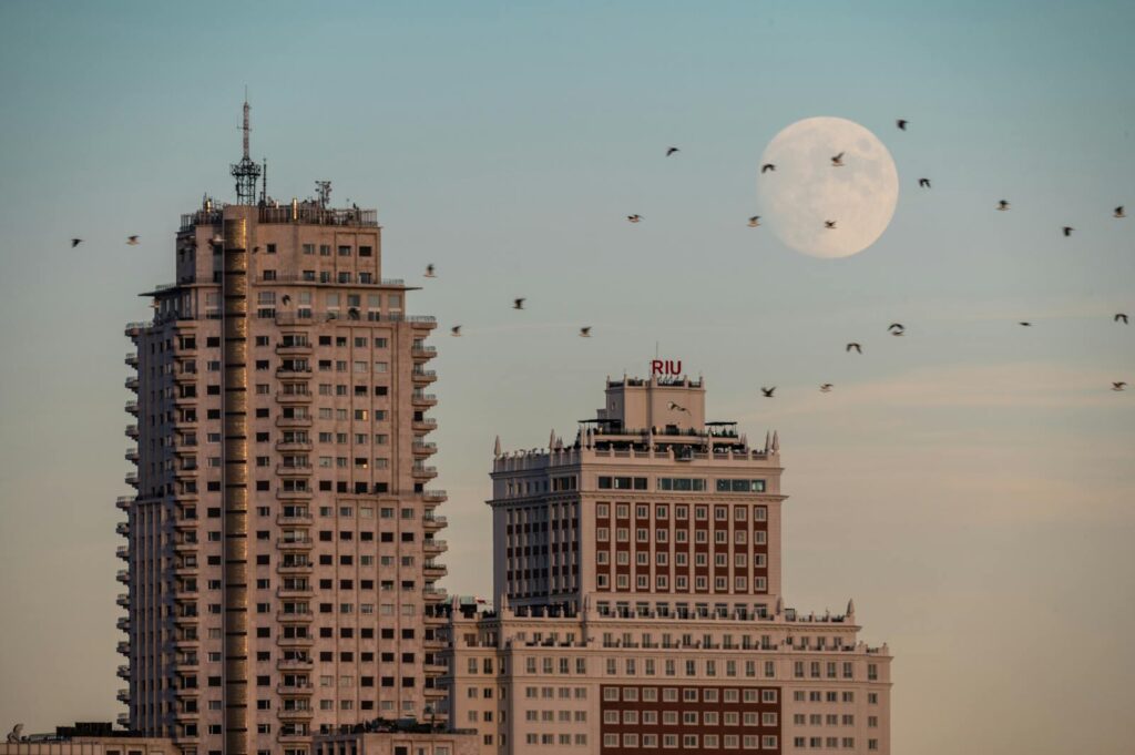 Majestic view of Edificio España in Madrid with a full moon and birds flying by.