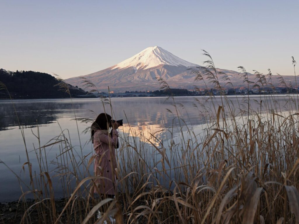 A woman captures the scenic beauty of Mount Fuji reflecting on a lake at sunset.