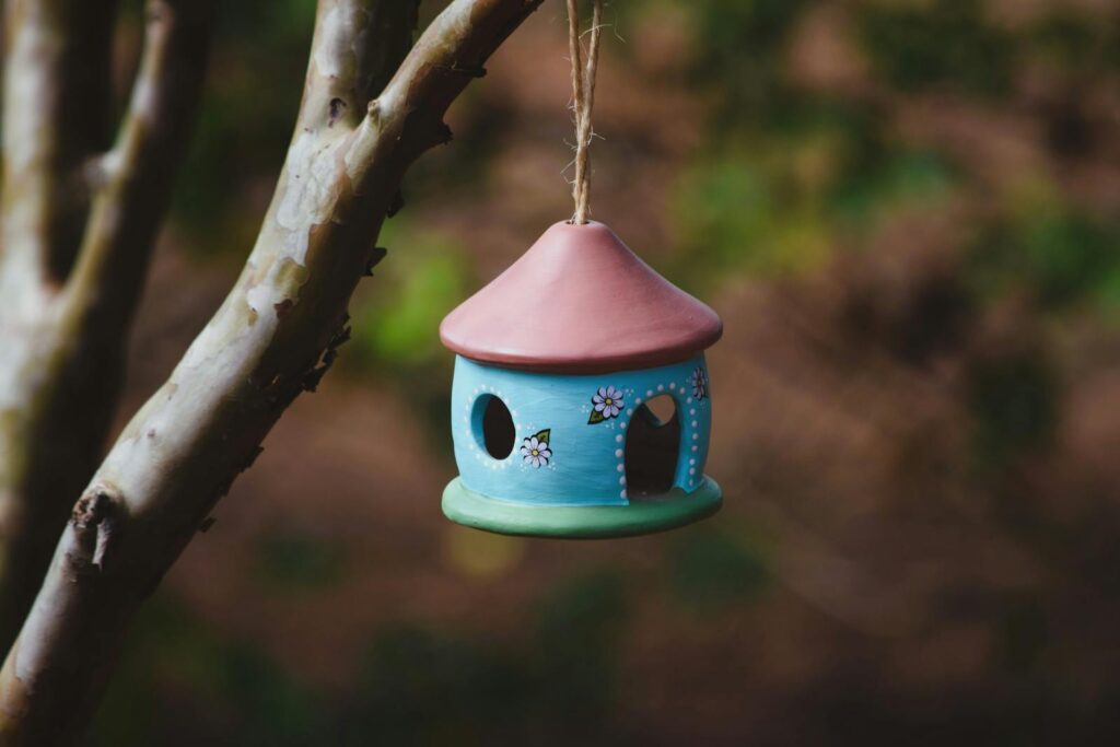 Vibrant ceramic birdhouse suspended on a tree branch in natural setting, ideal for garden decor.