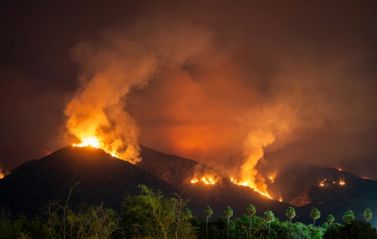 Flames engulf a hillside at night, creating a dramatic scene.