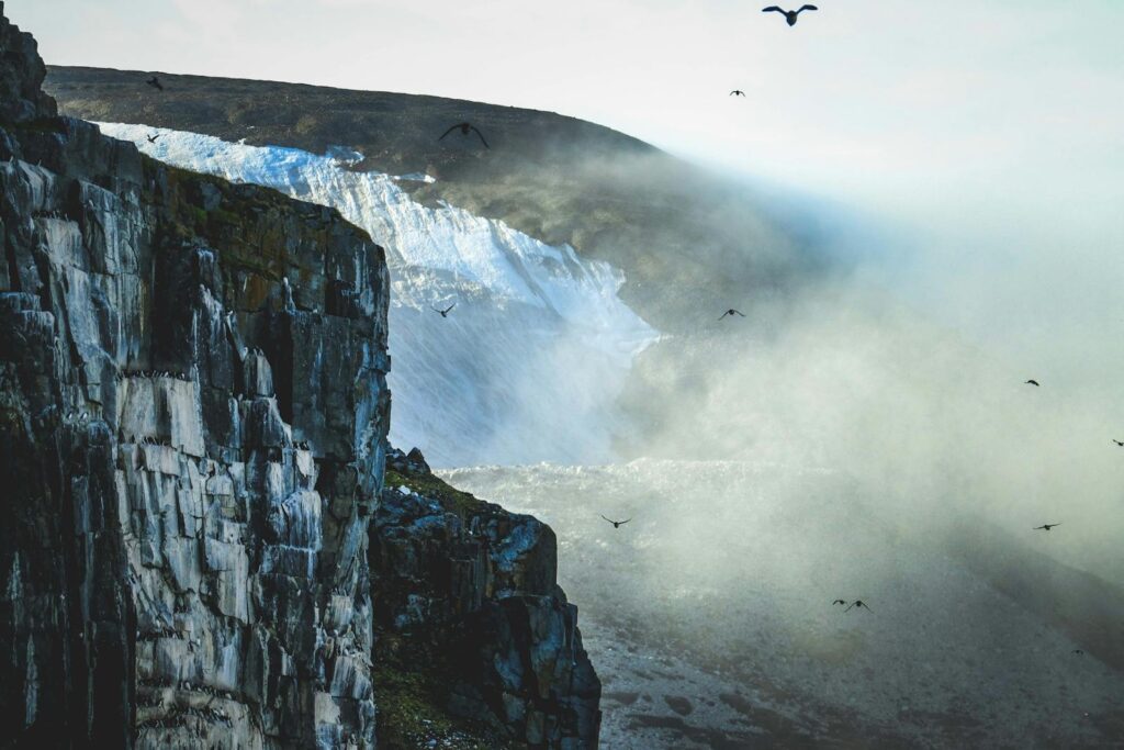 A breathtaking view of cliffs, glaciers, and birds in a misty landscape.