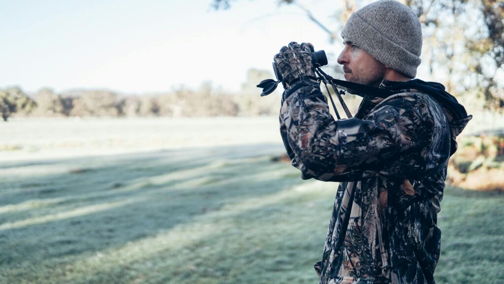 Man dressed in camo gear using binoculars