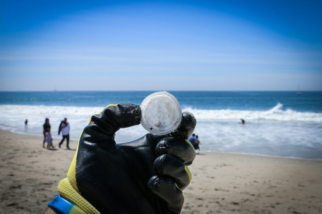 A gloved hand holds a piece of white plastic against a beach backdrop.