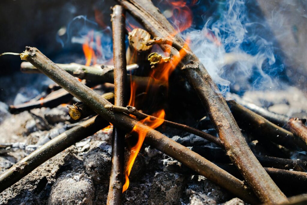A close-up view of a campfire with burning twigs, emitting warm flames and smoke.