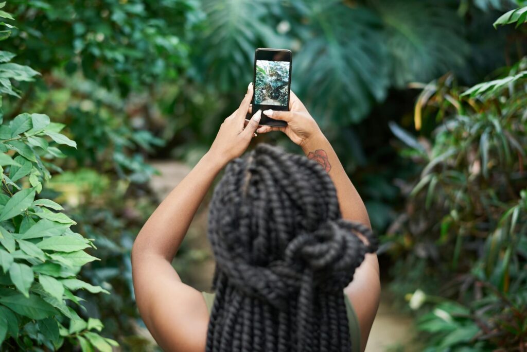 A woman is photographing lush greenery with a smartphone in an outdoor setting.