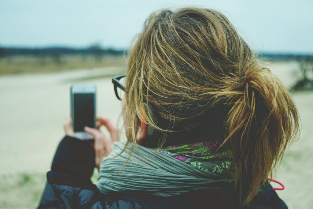 A woman taking a photo with a smartphone outdoors, capturing a scenic view.
