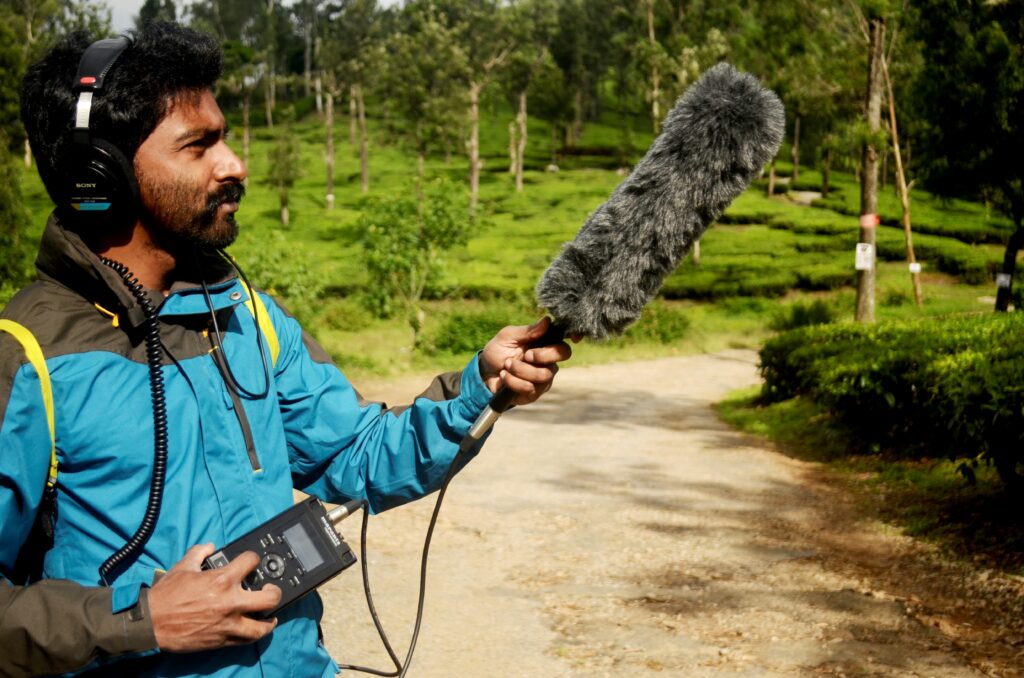 A researcher uses a boom microphone with a furry cover to record bird calls outdoors.