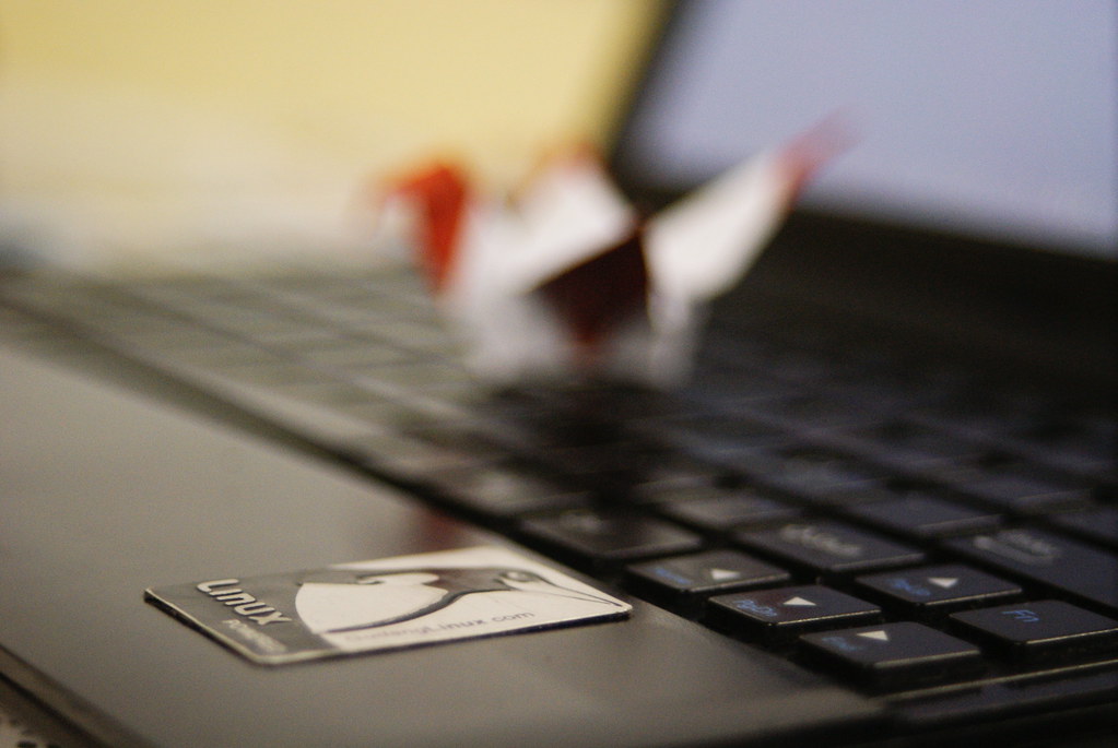  A blurred origami bird rests on a laptop near a Linux sticker.