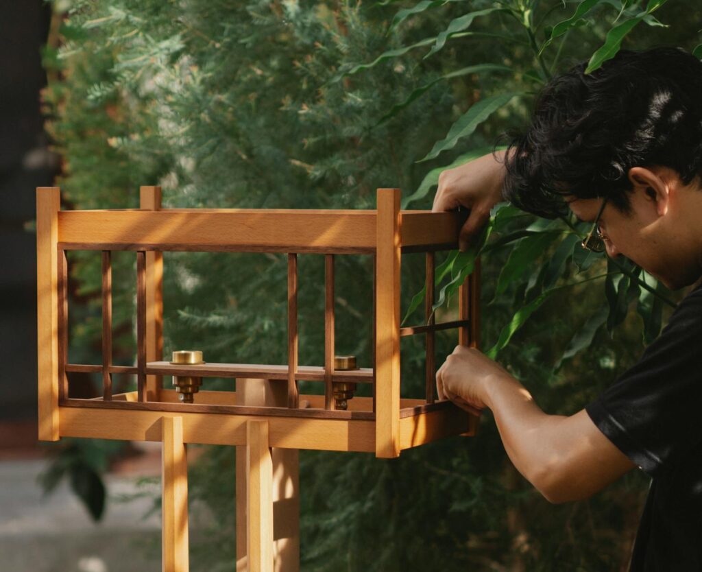 A craftsman carefully assembles a wooden bird feeder outdoors.