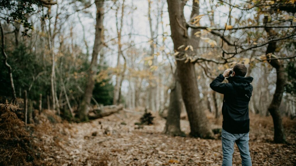 a man standing in a forest looking through binoculars