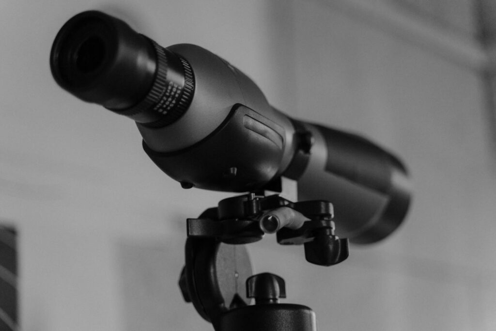 Detailed monochrome image of a modern telescope lens mounted on a tripod.