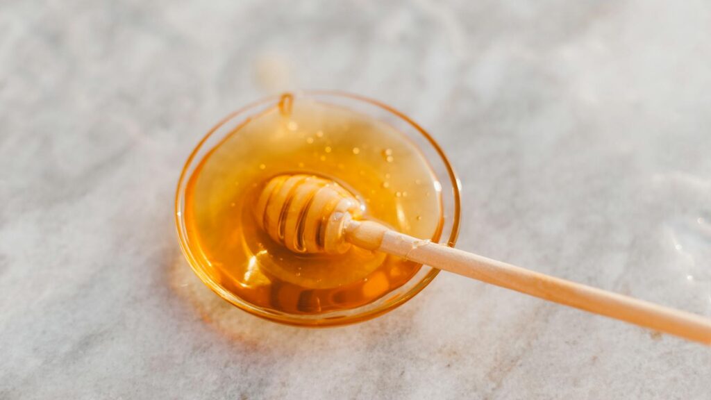 Wooden honey dripper coated with golden honey in a clear glass bow