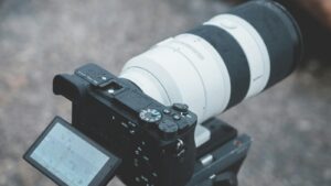 camera with a large telephoto zoom lens attached is mounted on a tripod.
