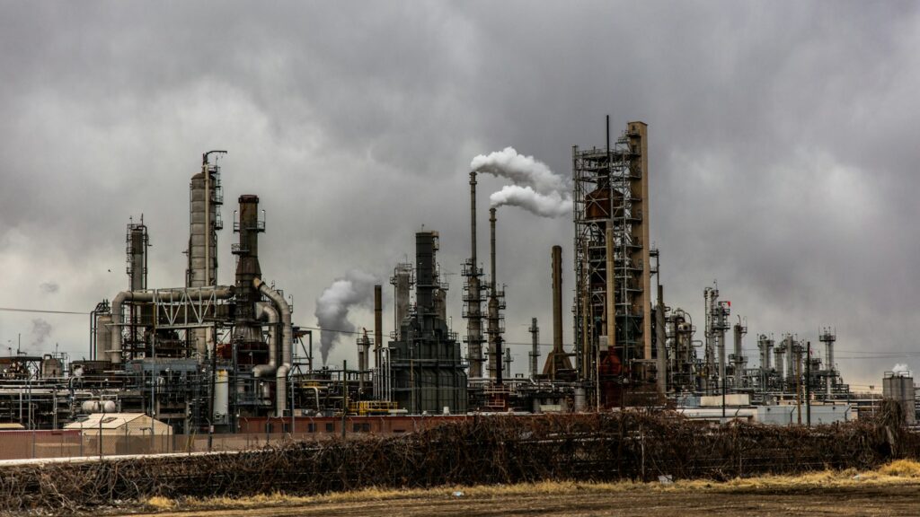 Industrial buildings with smoke stacks releasing emissions into cloudy sky