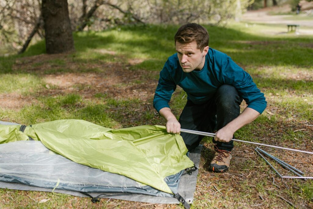 Man assembling a tent in a forest setting, preparing for a camping adventure.