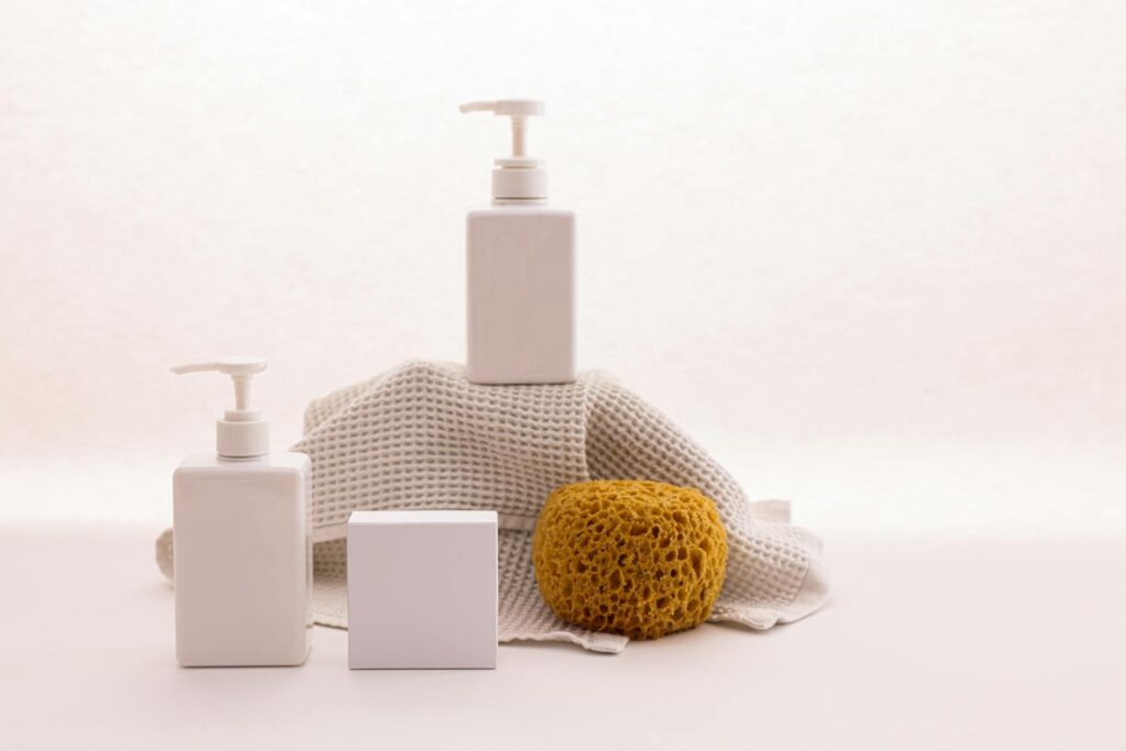 White pump bottles with a natural sponge on a textured cloth.