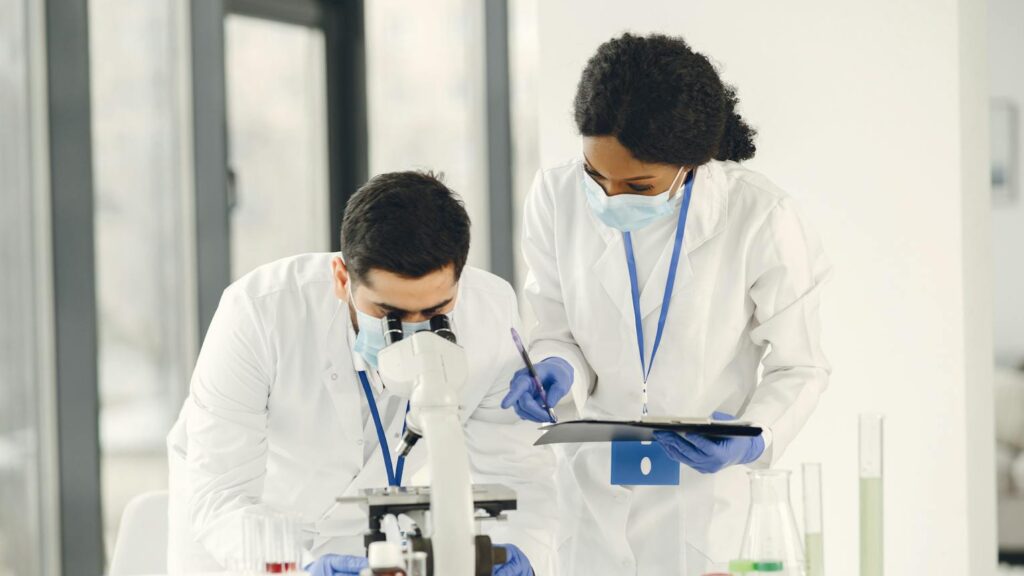 Two researchers in lab coats collaborating on experiment in laboratory