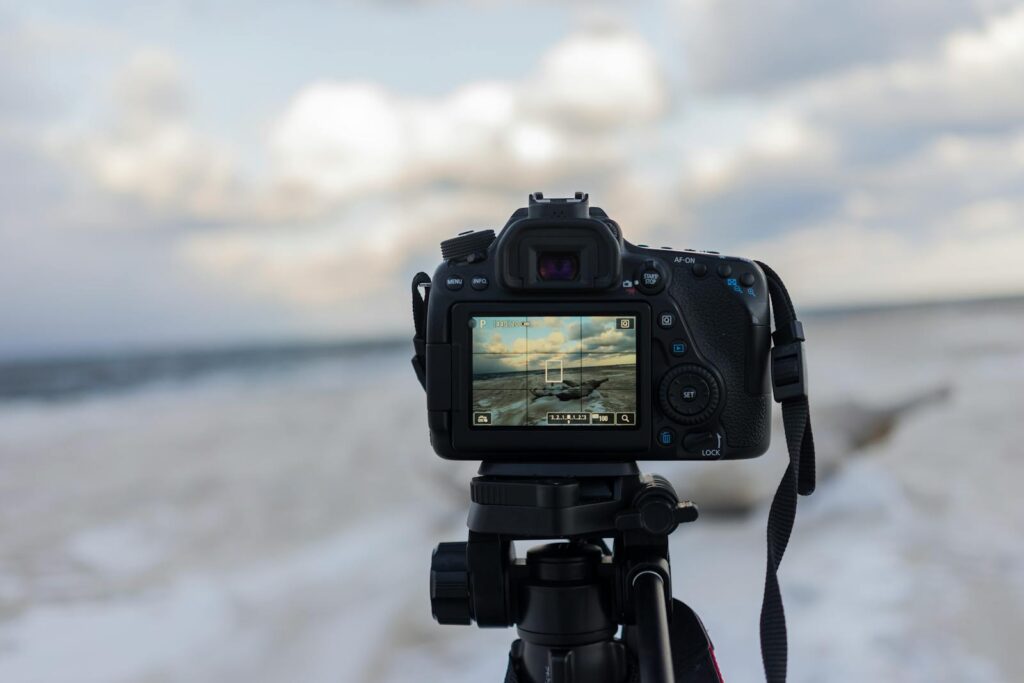 A DSLR camera on a tripod capturing a beach landscape with clouds.