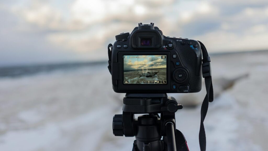A DSLR camera on a tripod capturing a beach landscape with clouds.