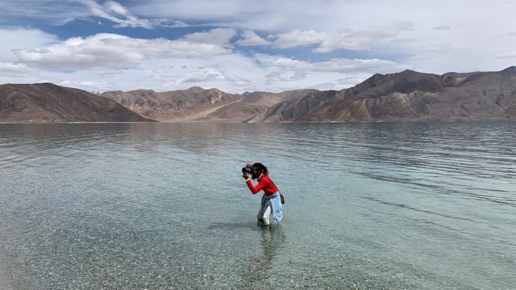Photographer stands in tranquil lake capturing stunning landscape view.
