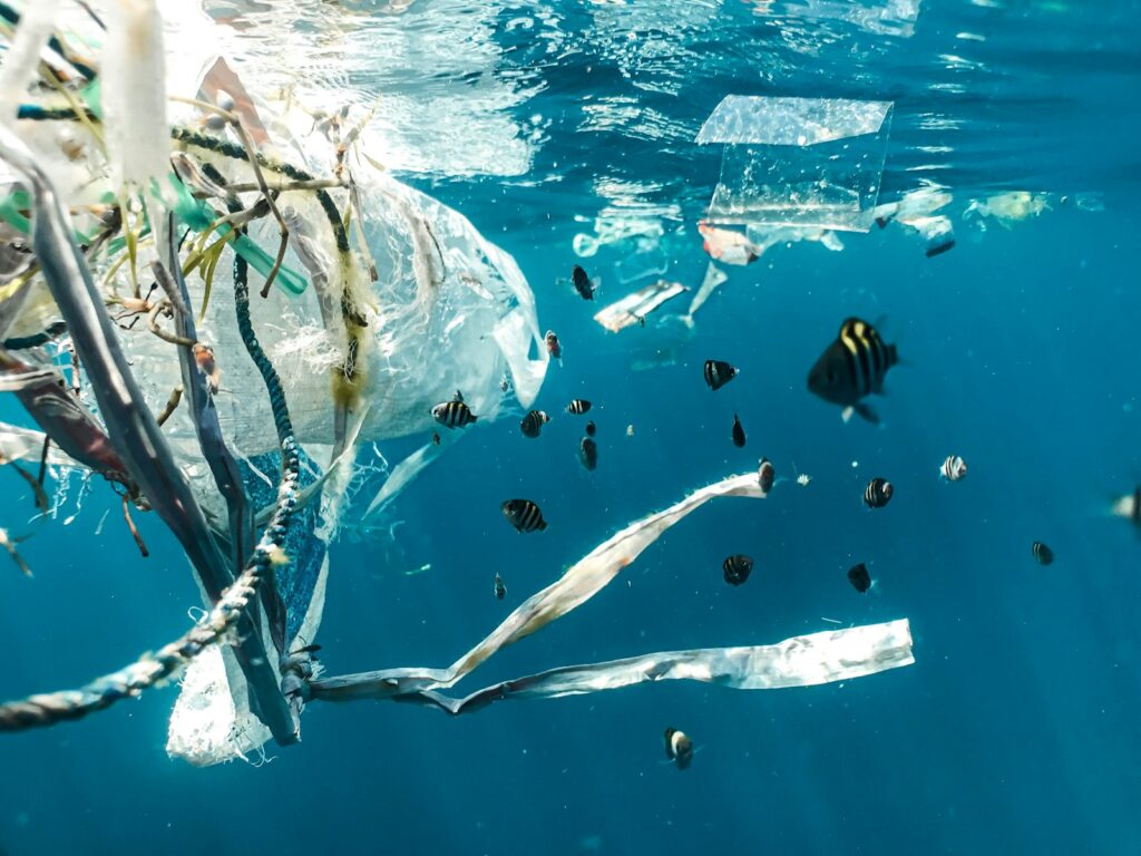 Plastic waste and debris float in the ocean with fish swimming nearby.